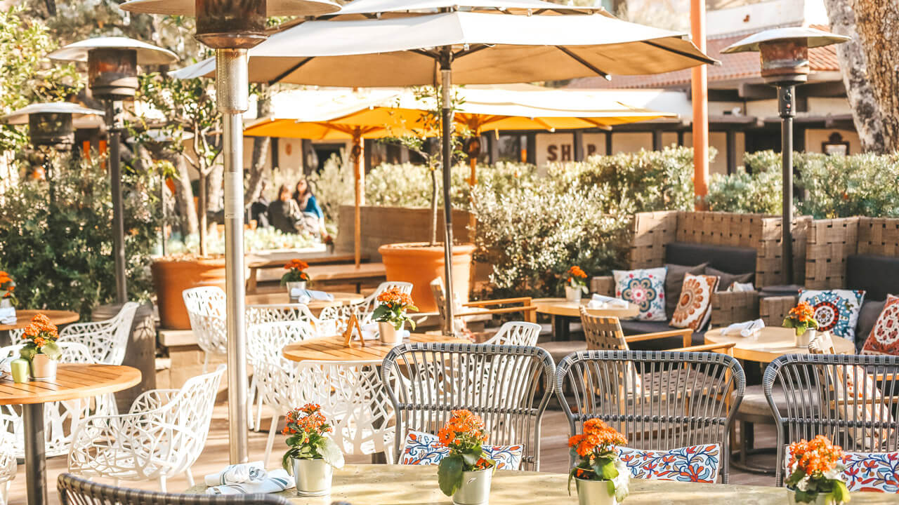 Outdoor dining with white chairs, benches, and umbrellas for shade